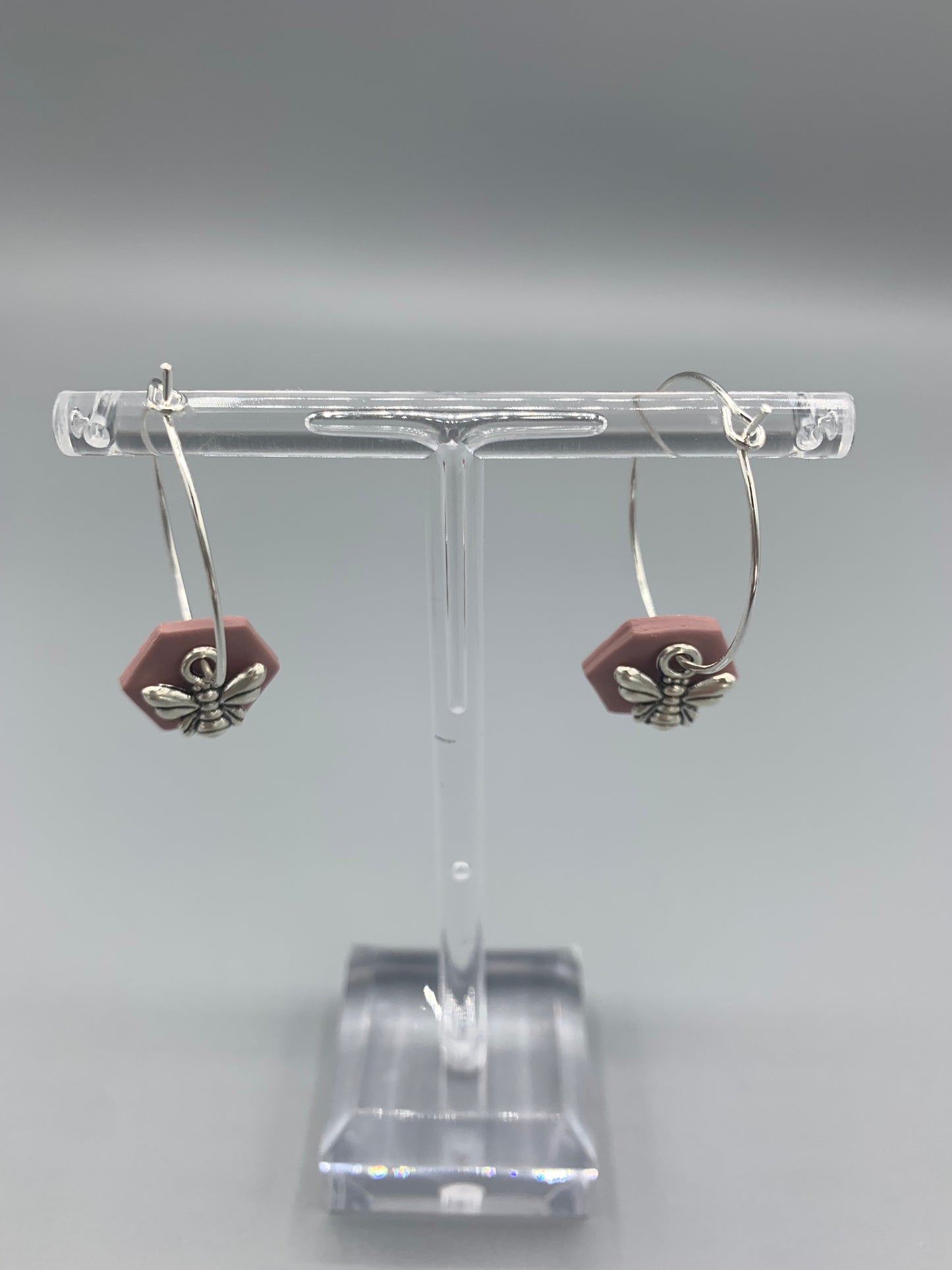 Alloy silver small bee charms on silver plated hoop earrings with an antique pink coloured fimo clay hexagonal disc behind the bee charm. 