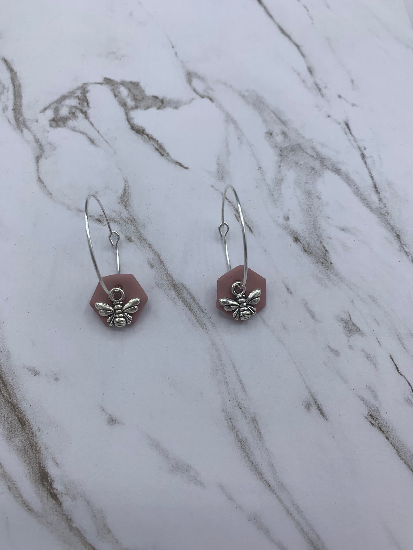 Alloy silver small bee charms on silver plated hoop earrings with an antique pink coloured fimo clay hexagonal disc behind the bee charm. 