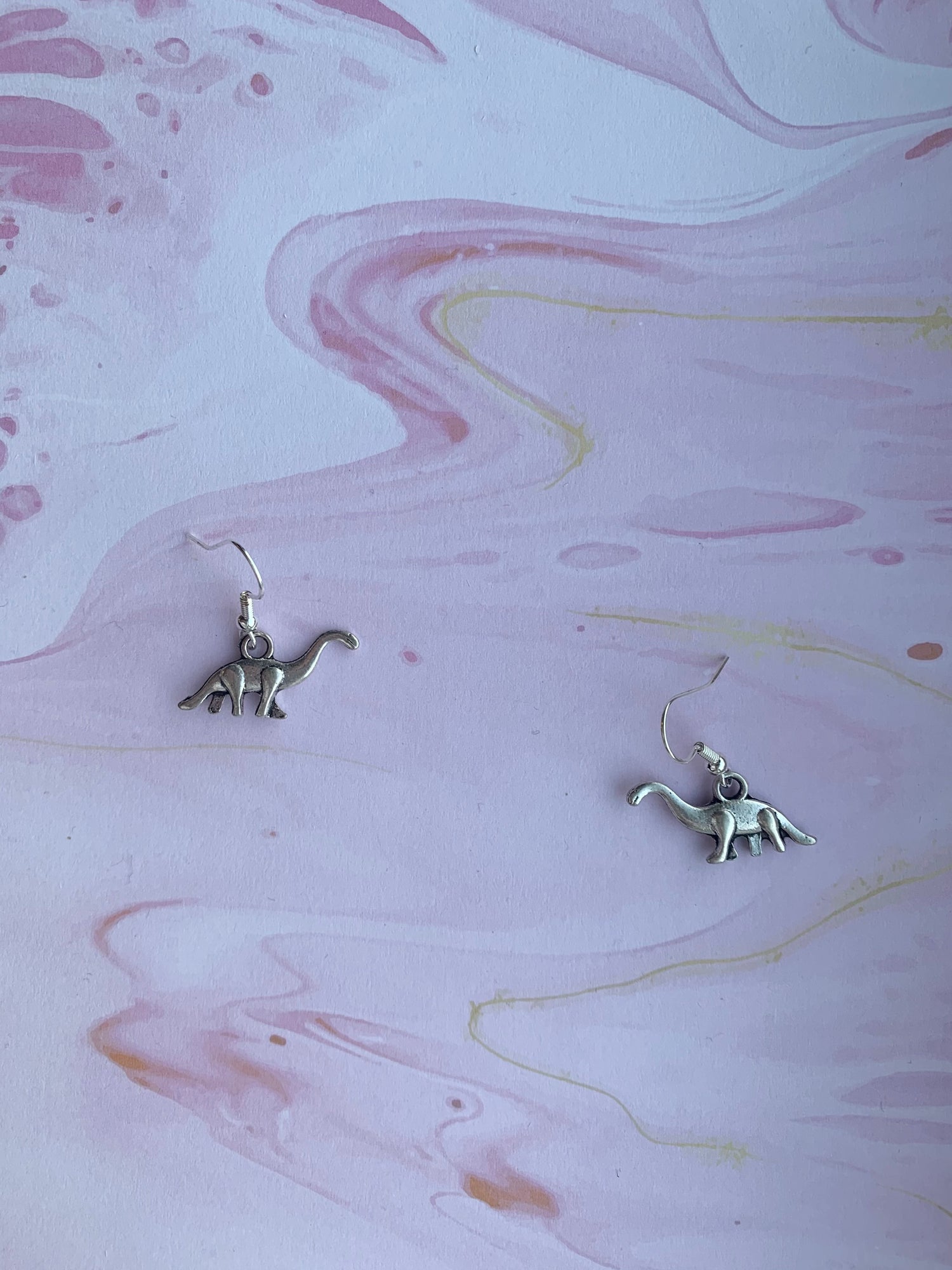 Alloy metal silver coloured brontosaurus charm on silver plated hoops. Dinosaur earrings. Animal earrings. Novelty earrings. 