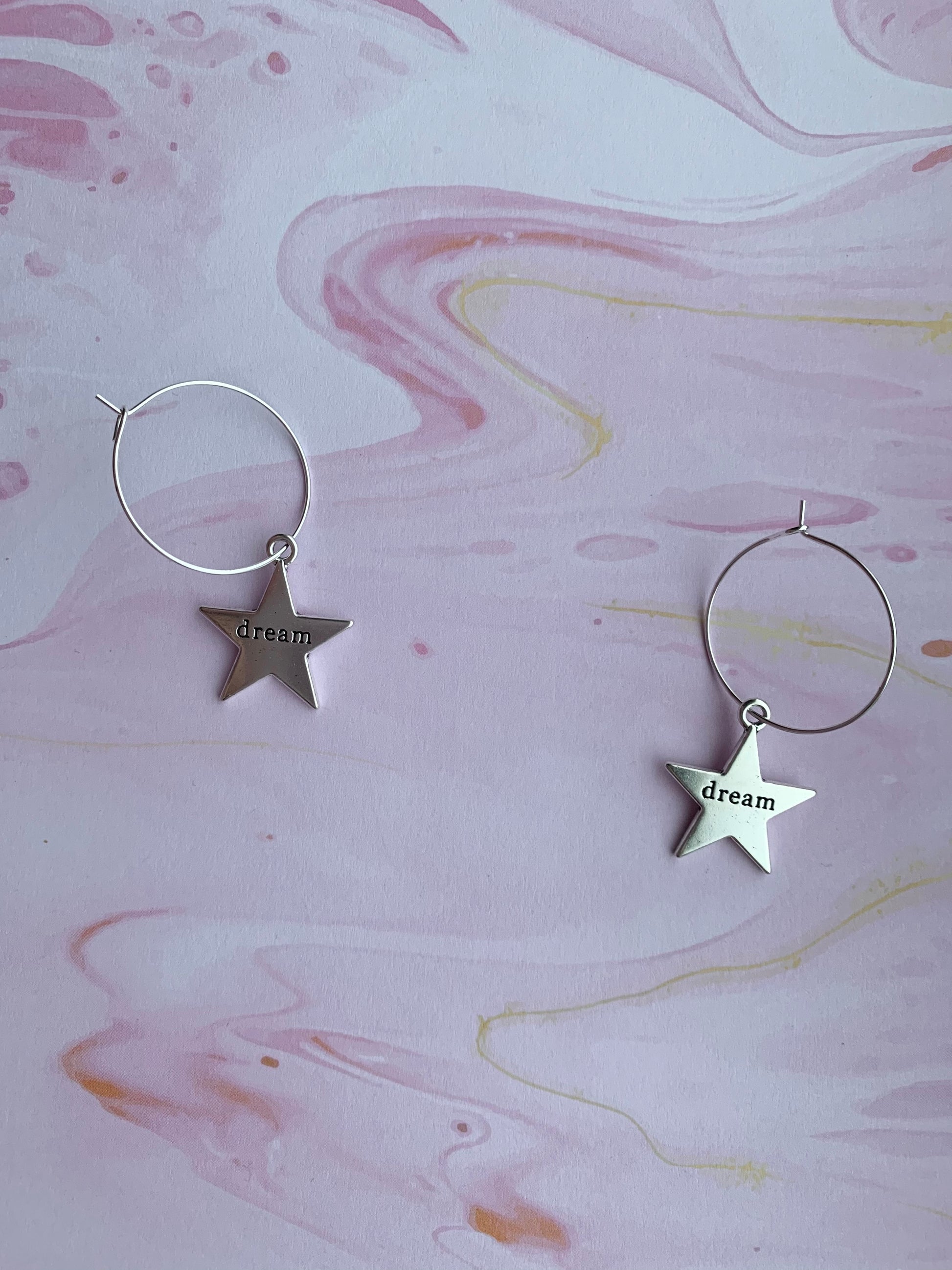 Large star silver coloured alloy charm with the word dream embossed across the centre on silver plated hoops. Hamilton earrings. Dream earrings. 