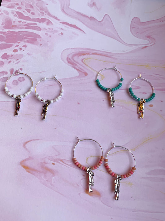 Colourful hoop earrings. Each pair has a alloy silver coloured parrot charm on silver plated hoops with different colour themed seed beads on the hoops. There is a white sparkle, turquoise and pink coral pair. Animal earrings. Bird earrings. 